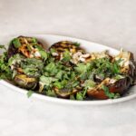 Gegrilde aubergine met verse kruiden op een wit bord, klaar om te serveren als vegetarisch bijgerecht