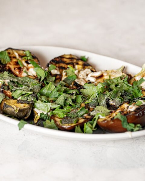 Gegrilde aubergine met verse kruiden op een wit bord, klaar om te serveren als vegetarisch bijgerecht