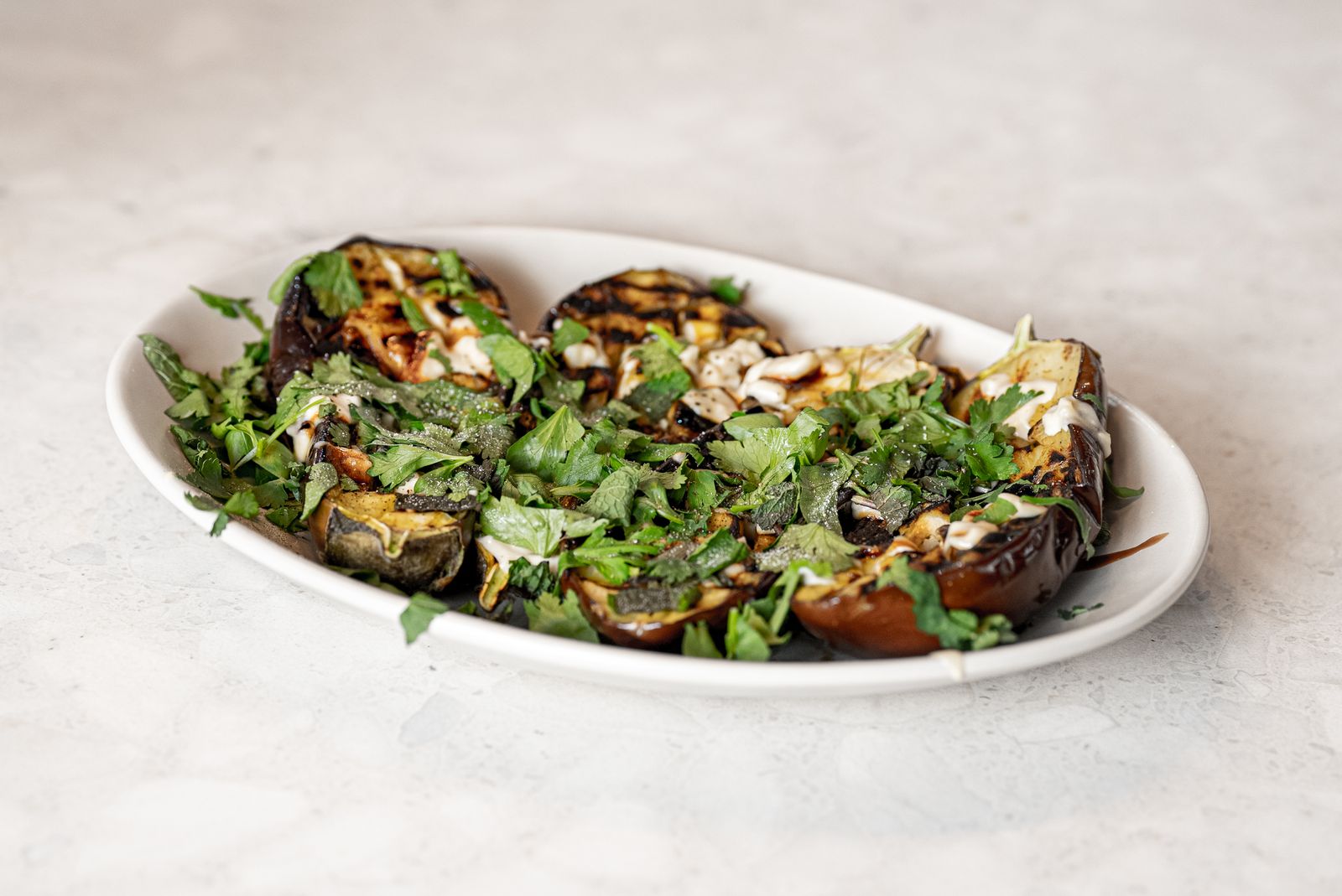 Gegrilde aubergine met verse kruiden op een wit bord, klaar om te serveren als vegetarisch bijgerecht