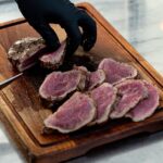 Kok snijdt medium-rare gegaard rundvlees in plakken op een houten snijplank