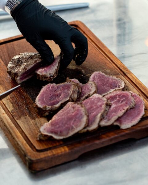 Kok snijdt medium-rare gegaard rundvlees in plakken op een houten snijplank