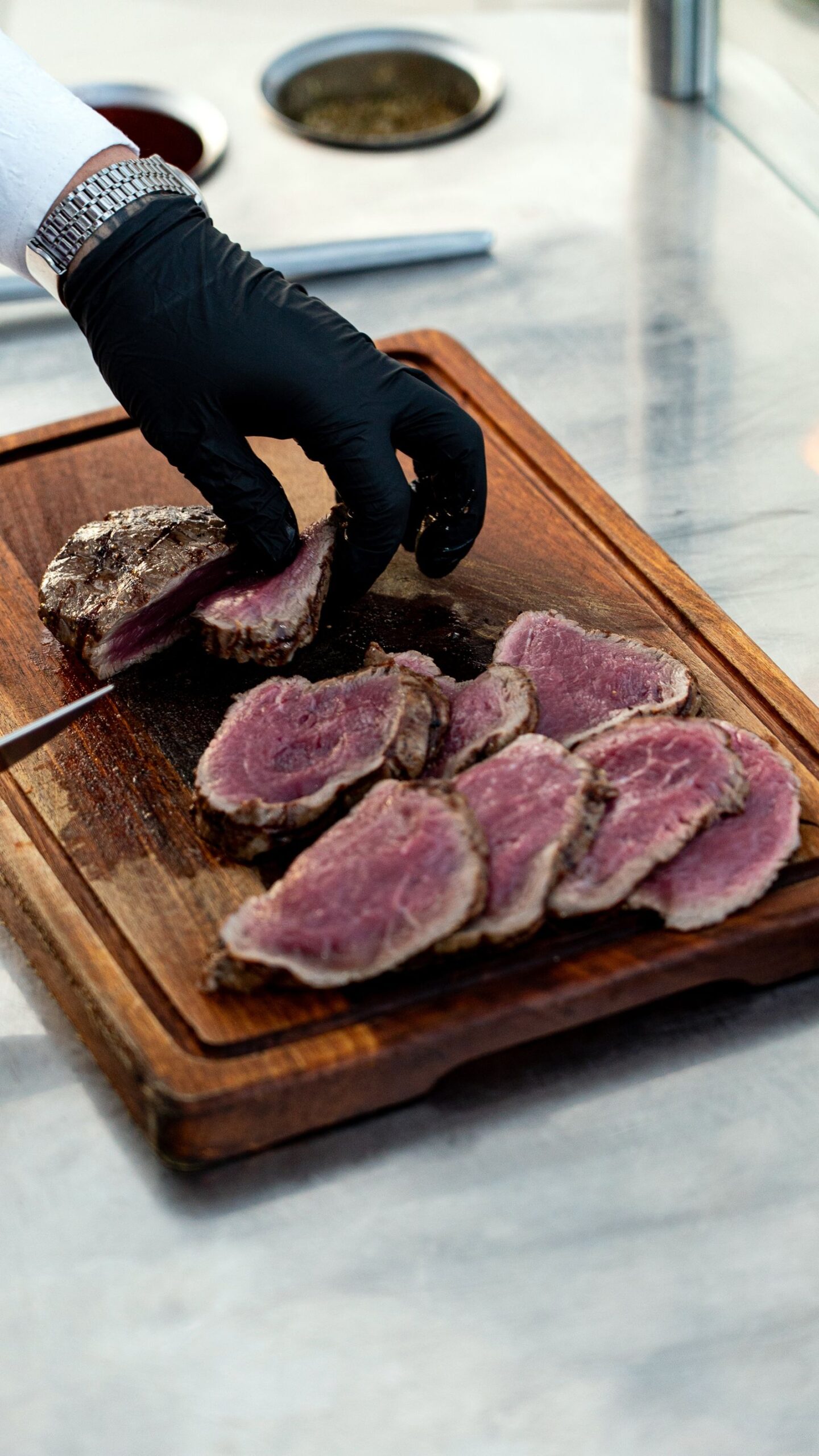 Kok snijdt medium-rare gegaard rundvlees in plakken op een houten snijplank