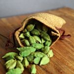 Jutezak vol verse groene kardemompeulen op een houten tafel