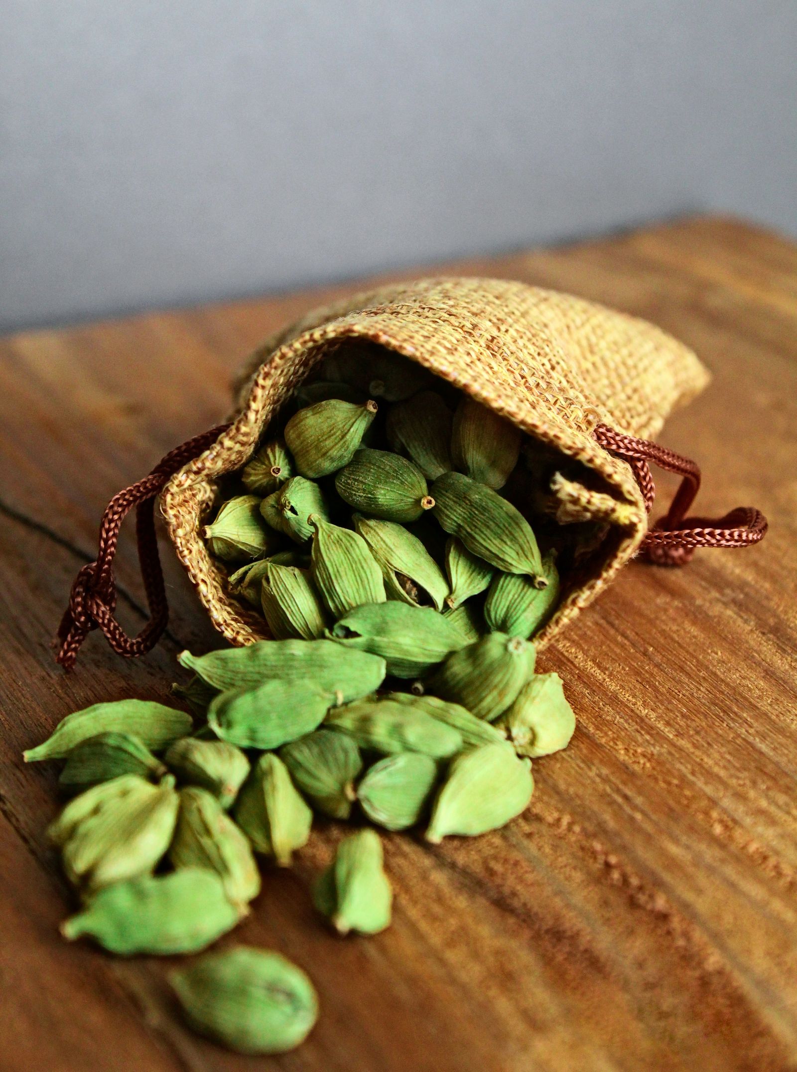 Jutezak vol verse groene kardemompeulen op een houten tafel